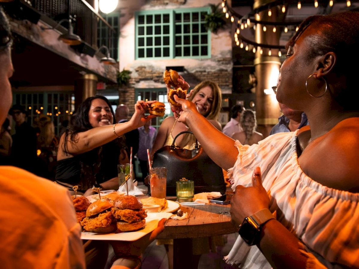 Friends raise their drinks in a toast at a lively dinner gathering, sharing laughs around a table of food and candles.