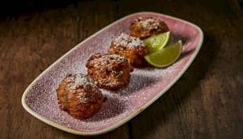 Sweet fried dough balls (kunafeh-like bites) dusted with sugar, served with lime wedges on a pink plate.