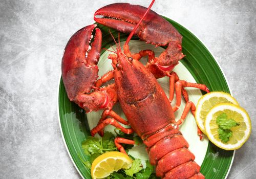 A plate of cooked lobster with claws and tails, garnished with cilantro and lemon slices.