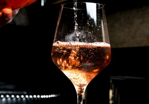 A bartender pours amber wine into a stemmed glass, sparkling as it fills under moody bar lighting.